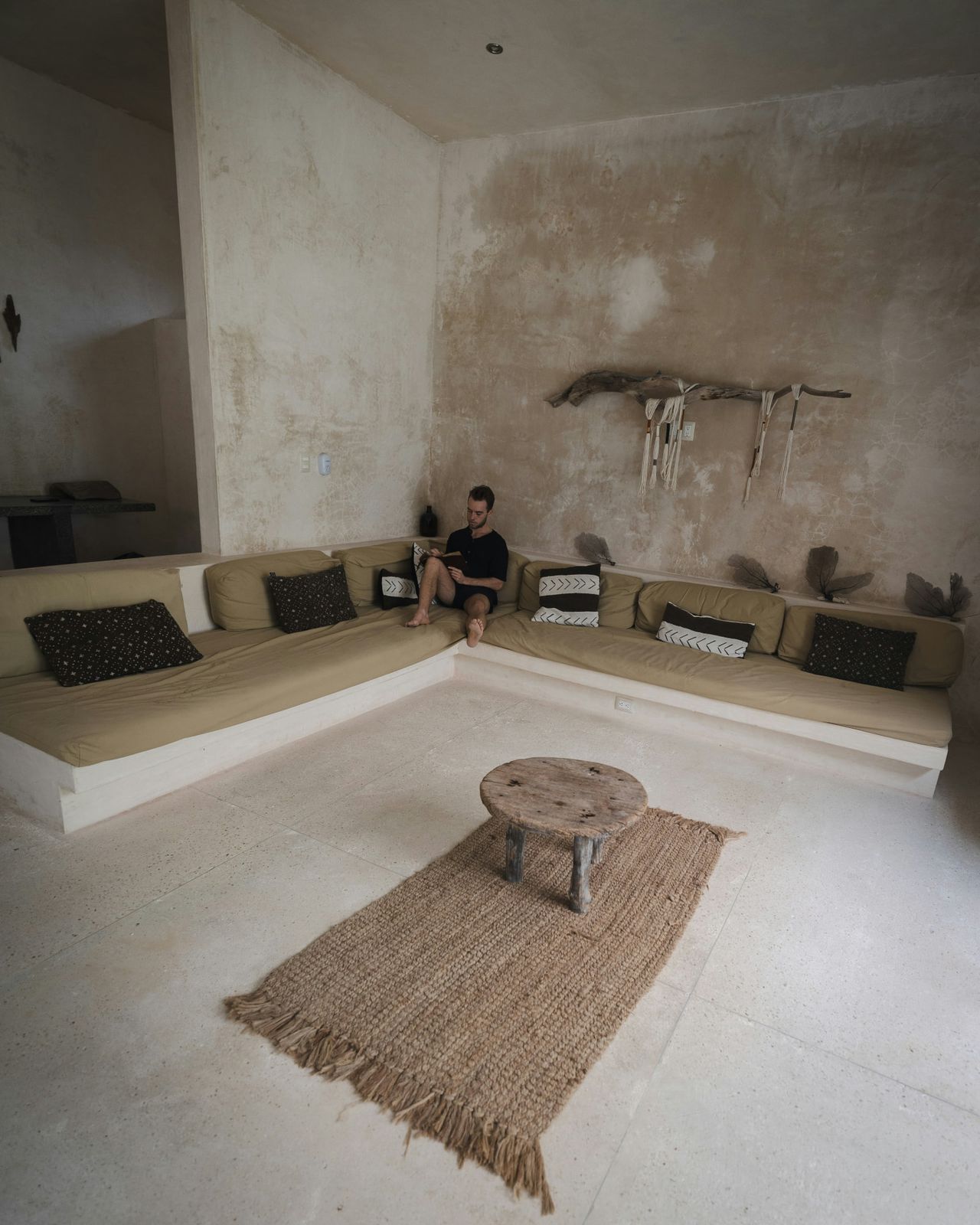 Chukum walled lounge with built in banquette, olive cushions, driftwood object and a jute rug on polished concrete.