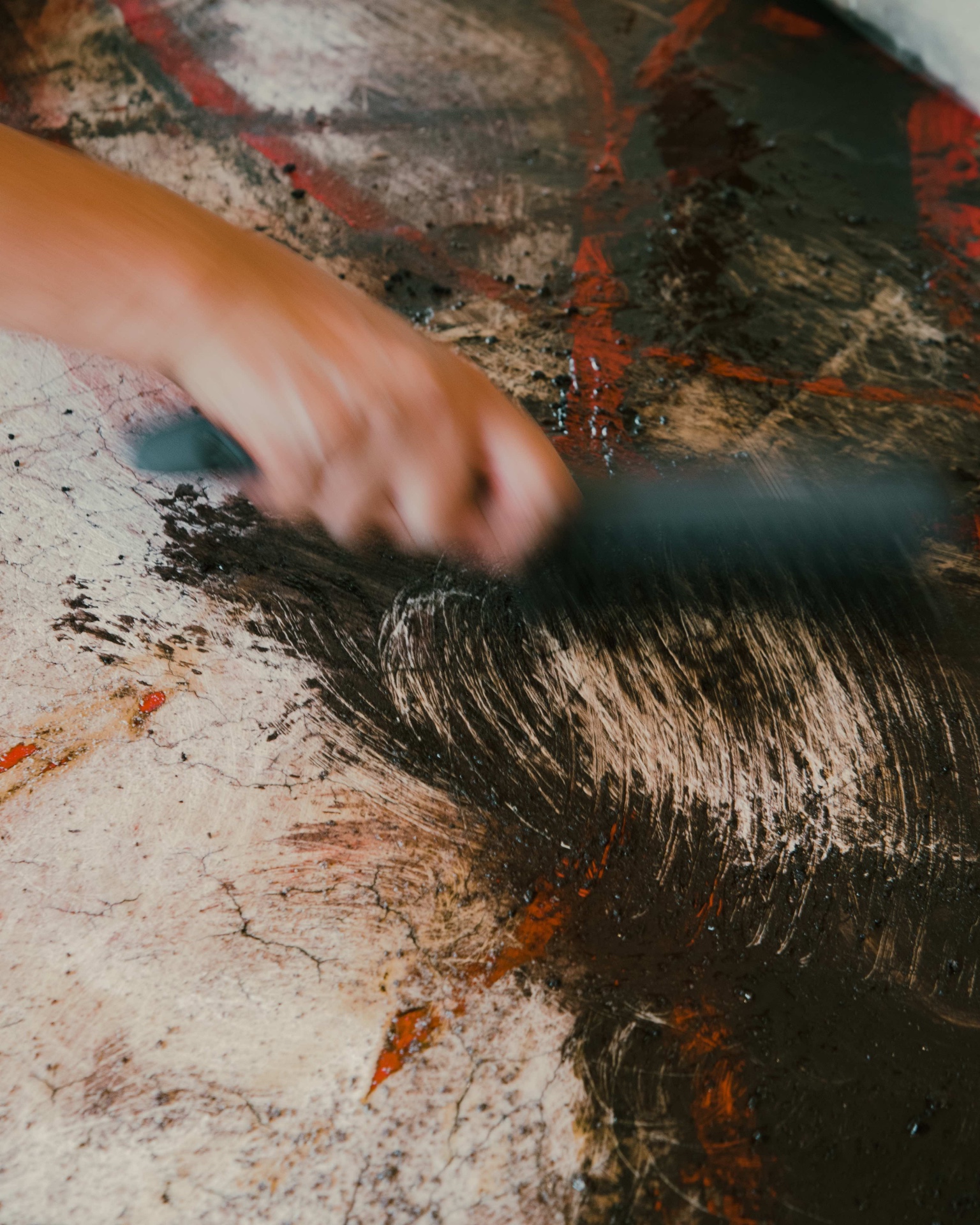 Artist painting freehand on a wall during a Tulum Art Club production, brush in hand and paint containers on the floor.